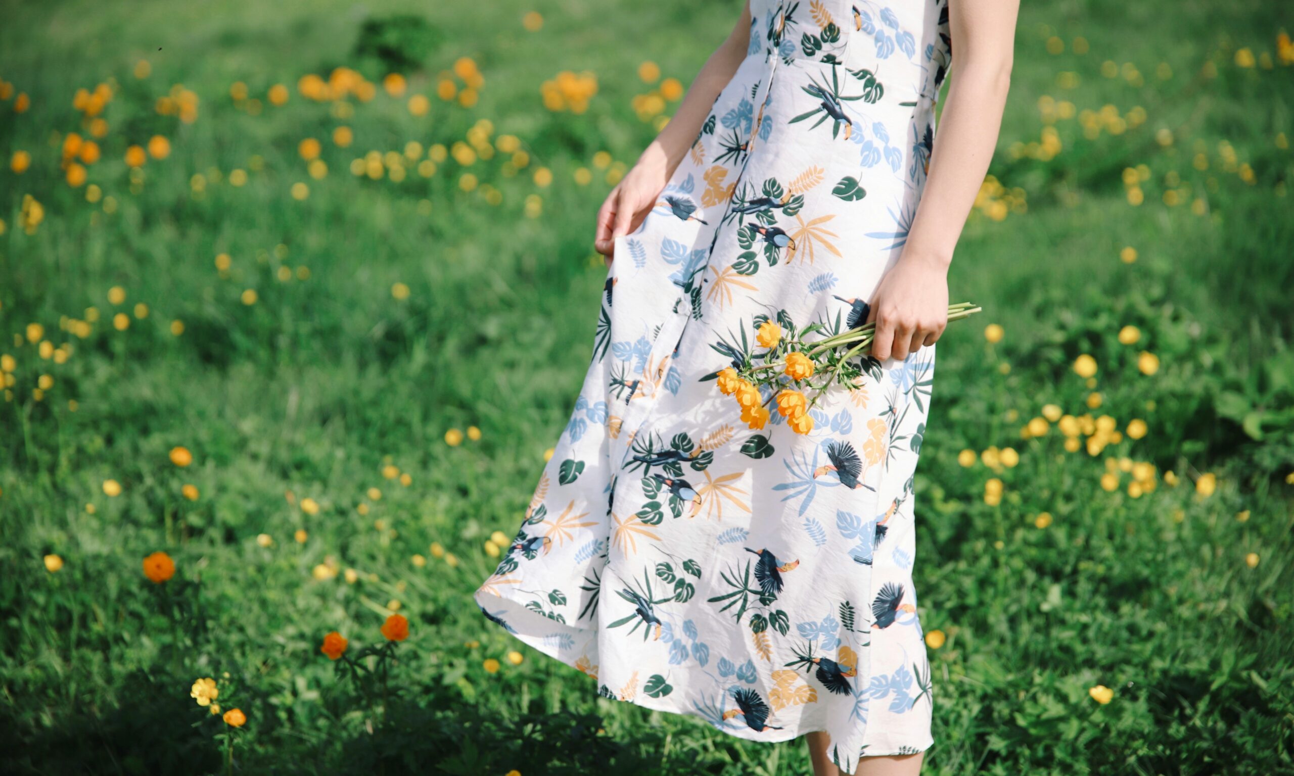 A woman in a sundress, holding a bouquet in a floral meadow.